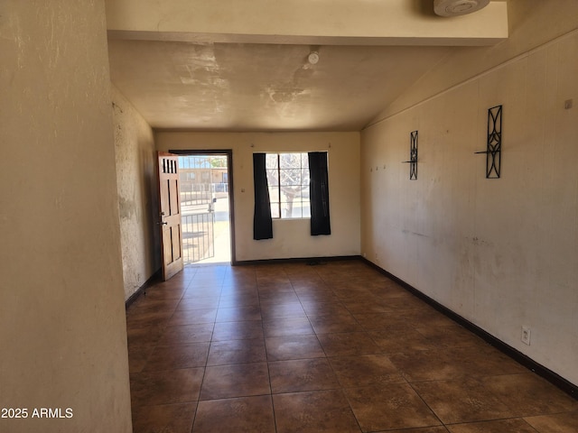 spare room featuring lofted ceiling, dark tile patterned floors, and baseboards