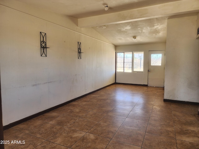 empty room with vaulted ceiling with beams, wooden walls, and baseboards