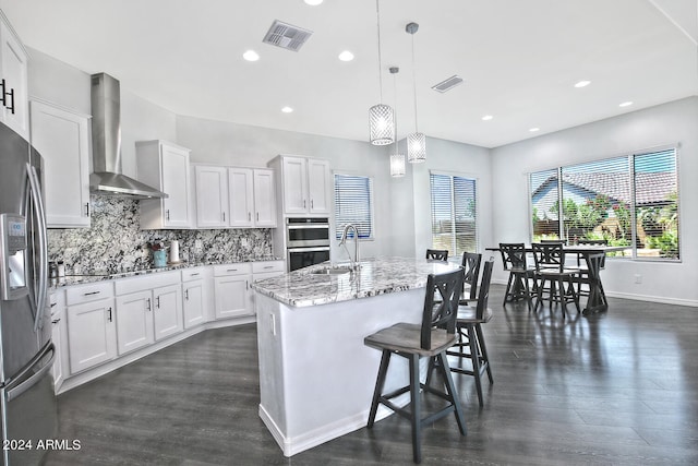 kitchen with dark wood-type flooring, wall chimney range hood, light stone countertops, and white cabinetry