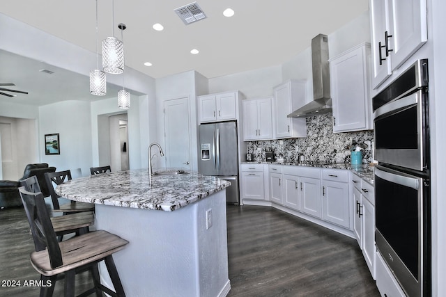 kitchen featuring dark hardwood / wood-style flooring, decorative light fixtures, appliances with stainless steel finishes, tasteful backsplash, and wall chimney range hood