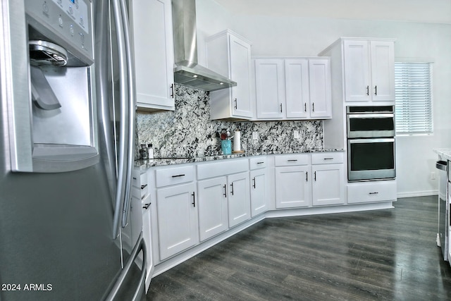 kitchen with stainless steel appliances, white cabinetry, light stone countertops, wall chimney range hood, and dark hardwood / wood-style flooring