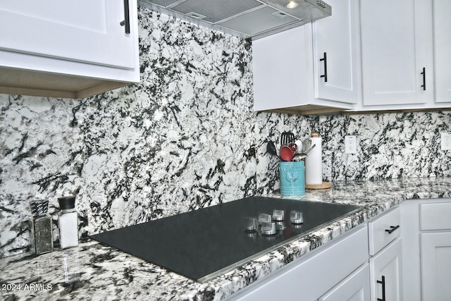 kitchen with light stone counters, black electric cooktop, white cabinets, and custom exhaust hood