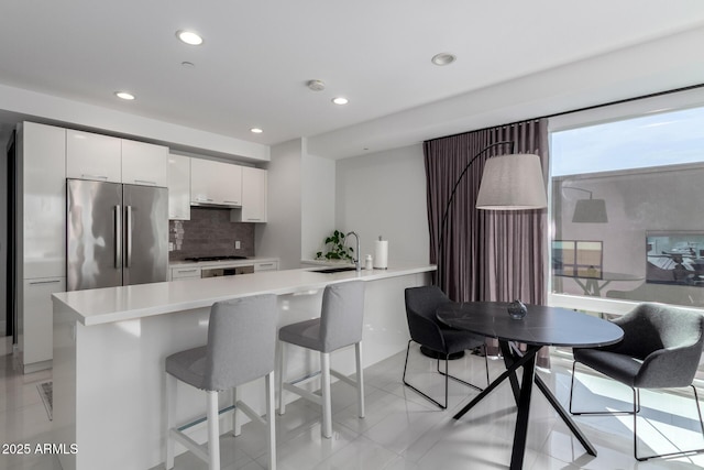 kitchen featuring sink, stainless steel fridge, white cabinets, a breakfast bar area, and decorative backsplash