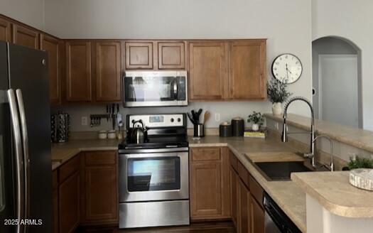 kitchen with stainless steel appliances, a peninsula, light countertops, a sink, and arched walkways