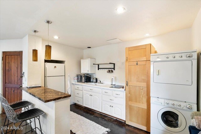 kitchen featuring hanging light fixtures, stacked washing maching and dryer, white cabinetry, a breakfast bar, and white fridge