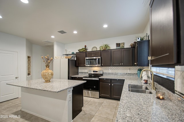 kitchen featuring dark brown cabinetry, a kitchen island, a sink, stainless steel appliances, and backsplash