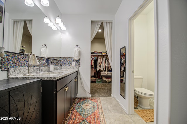 full bath featuring double vanity, a spacious closet, decorative backsplash, toilet, and a sink