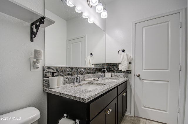 bathroom featuring toilet, a sink, decorative backsplash, and double vanity