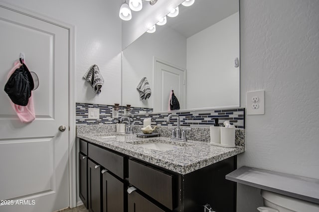 bathroom with double vanity, decorative backsplash, a sink, and a textured wall