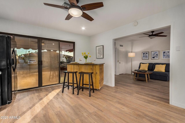 interior space with kitchen peninsula, a kitchen bar, black fridge, ceiling fan, and hardwood / wood-style flooring