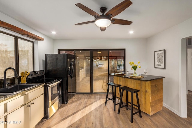 kitchen with a kitchen breakfast bar, light wood-type flooring, stainless steel range with electric stovetop, ceiling fan, and sink