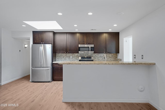 kitchen featuring light stone countertops, dark brown cabinets, kitchen peninsula, and appliances with stainless steel finishes