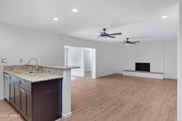 kitchen featuring stainless steel dishwasher, sink, light wood-type flooring, light stone counters, and a fireplace