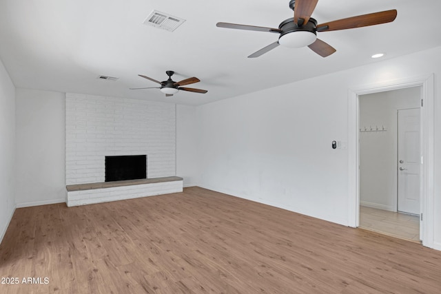 unfurnished living room featuring ceiling fan, light wood-type flooring, and a brick fireplace