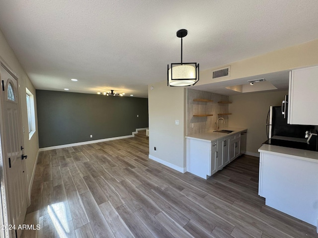 kitchen with white cabinetry, sink, pendant lighting, wood-type flooring, and a textured ceiling