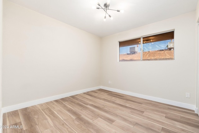 spare room featuring light wood-style flooring, baseboards, and a notable chandelier