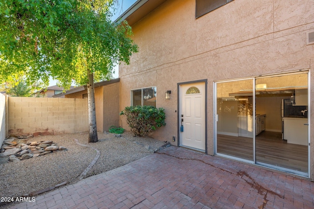 view of exterior entry featuring a patio, fence, visible vents, and stucco siding