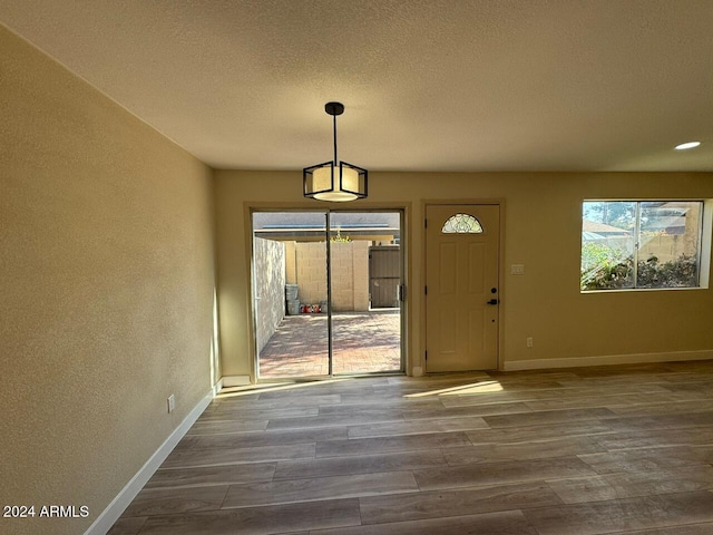 interior space with a textured wall, a textured ceiling, baseboards, and wood finished floors