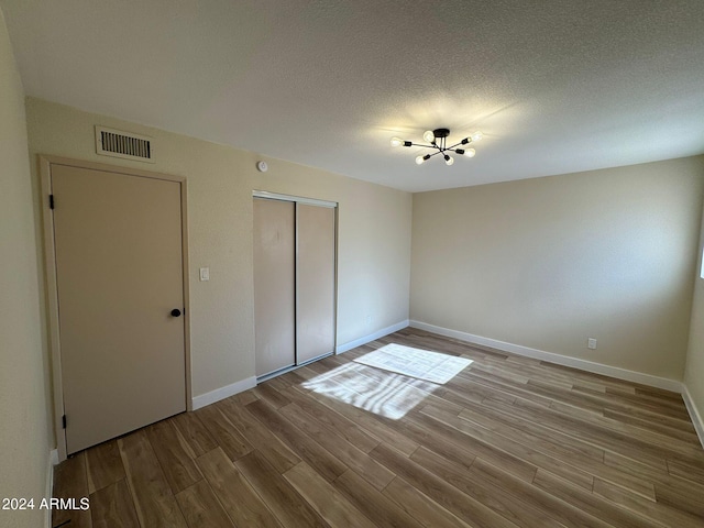 unfurnished bedroom with baseboards, visible vents, wood finished floors, a textured ceiling, and a closet