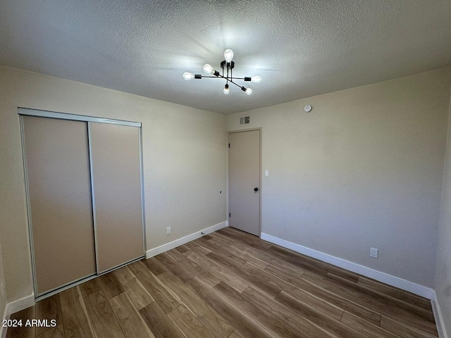 unfurnished bedroom with a closet, baseboards, visible vents, wood finished floors, and a notable chandelier