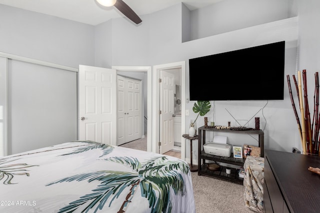 bedroom with a high ceiling, ceiling fan, connected bathroom, light colored carpet, and a closet