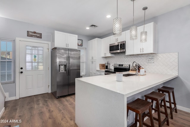 kitchen featuring decorative light fixtures, white cabinetry, kitchen peninsula, and appliances with stainless steel finishes