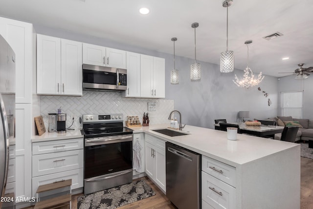 kitchen featuring kitchen peninsula, appliances with stainless steel finishes, sink, white cabinets, and hanging light fixtures