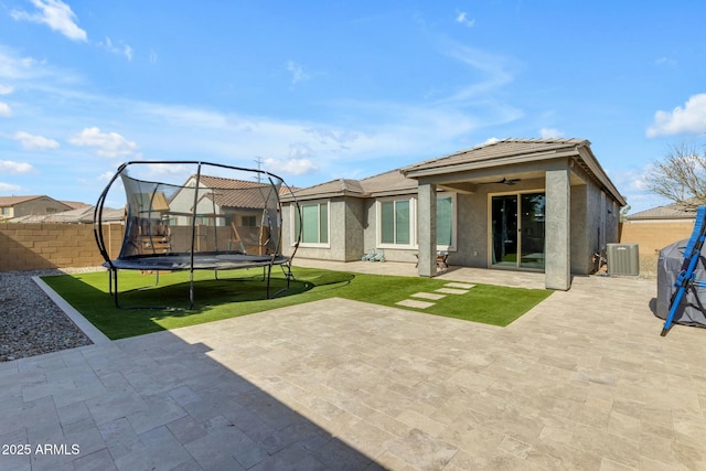 rear view of property featuring stucco siding, a ceiling fan, a trampoline, cooling unit, and a patio area