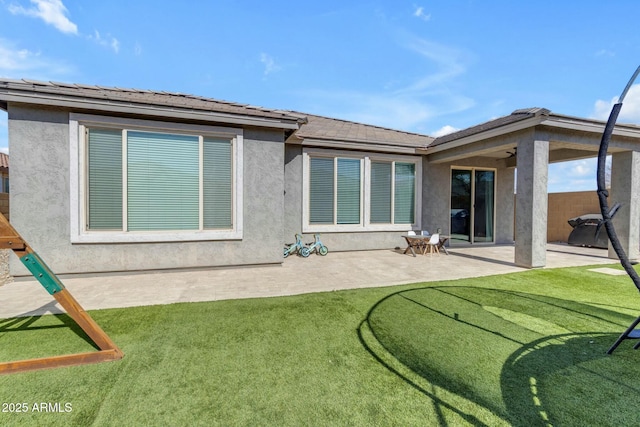 rear view of house featuring a yard, a patio area, and stucco siding