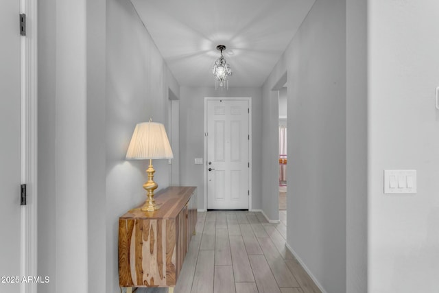 hall with a notable chandelier, baseboards, and light wood-style floors