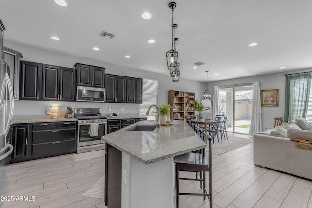 kitchen with light stone counters, visible vents, a sink, stainless steel appliances, and dark cabinets