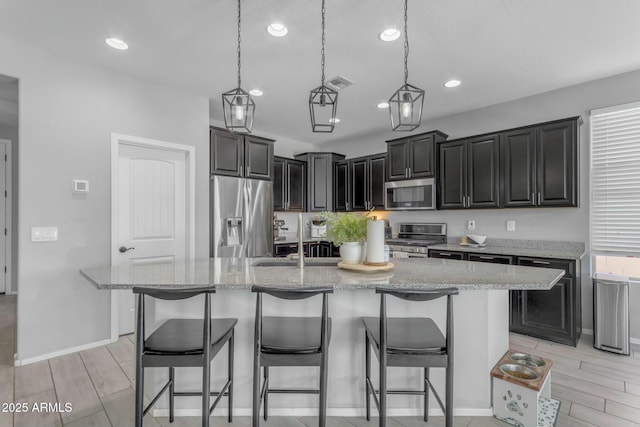 kitchen with a breakfast bar area, light stone countertops, stainless steel appliances, and a sink