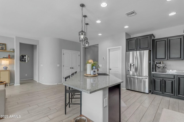 kitchen with light stone counters, wood finish floors, stainless steel refrigerator with ice dispenser, and a sink