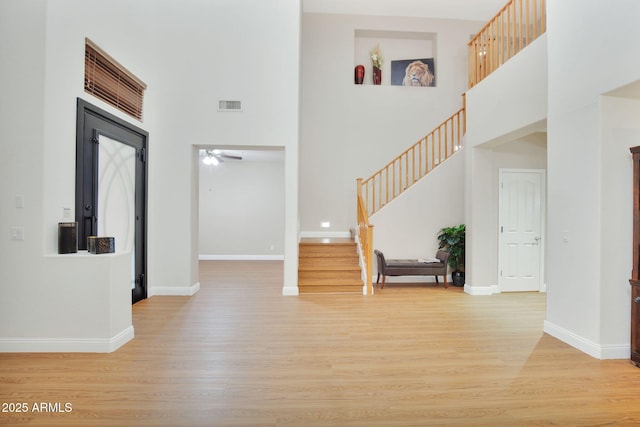 foyer featuring visible vents, baseboards, a towering ceiling, light wood-style flooring, and stairway