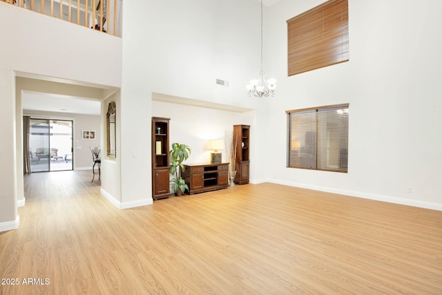 living room featuring visible vents, a high ceiling, an inviting chandelier, light wood-type flooring, and baseboards