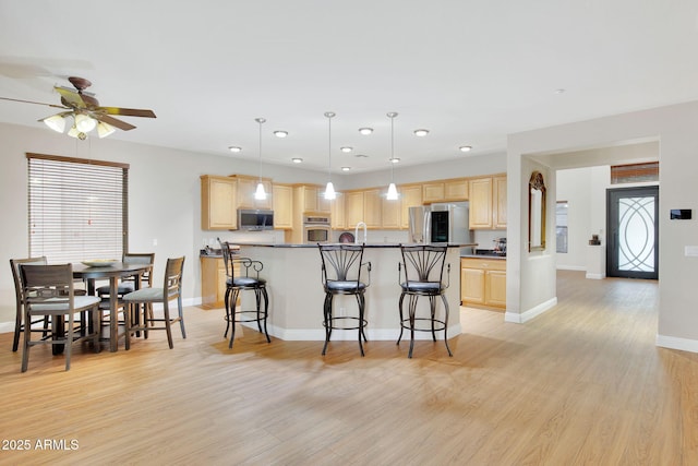 kitchen featuring dark countertops, appliances with stainless steel finishes, a breakfast bar, light wood-type flooring, and light brown cabinets