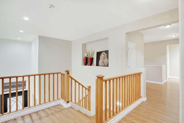 hallway with recessed lighting, wood finished floors, an upstairs landing, and baseboards