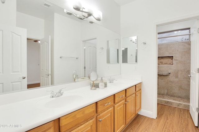 bathroom featuring a sink, double vanity, a tile shower, and wood finished floors