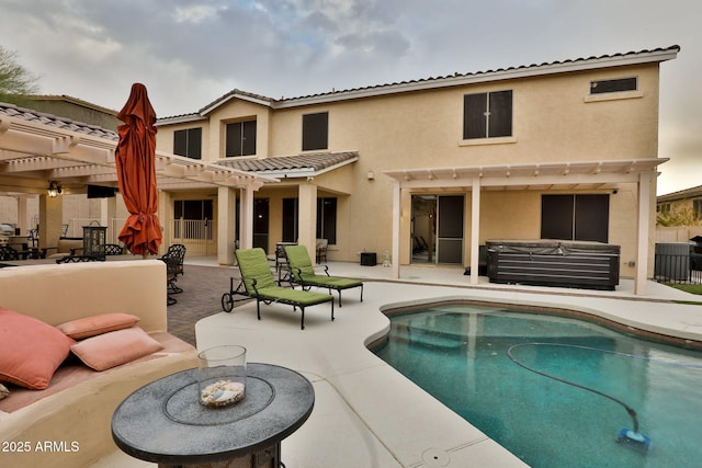 rear view of house with a hot tub, a patio, a pergola, and stucco siding