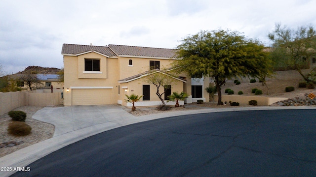 view of front of home with stucco siding, concrete driveway, an attached garage, fence, and a tiled roof