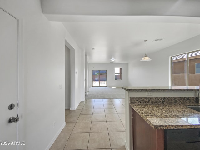 kitchen with light tile patterned floors, baseboards, dark stone counters, a sink, and dishwasher