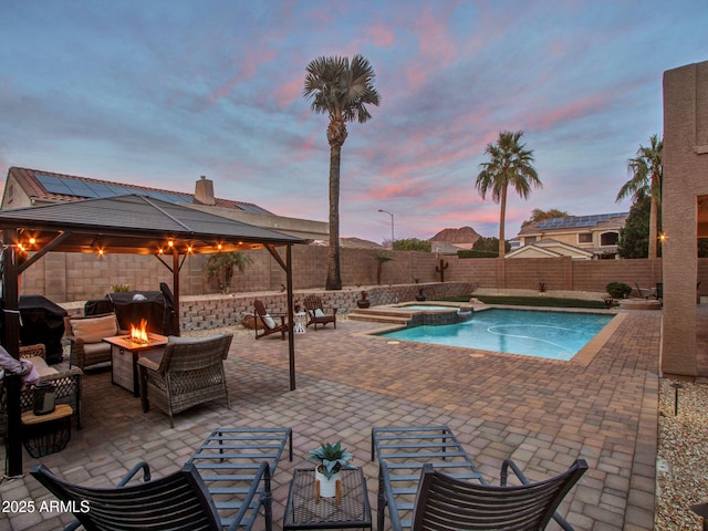 pool at dusk with a gazebo, an in ground hot tub, a patio area, and a fire pit