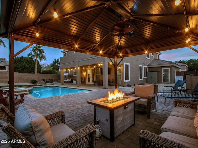 pool at dusk featuring a gazebo, a patio area, and an outdoor living space with a fire pit