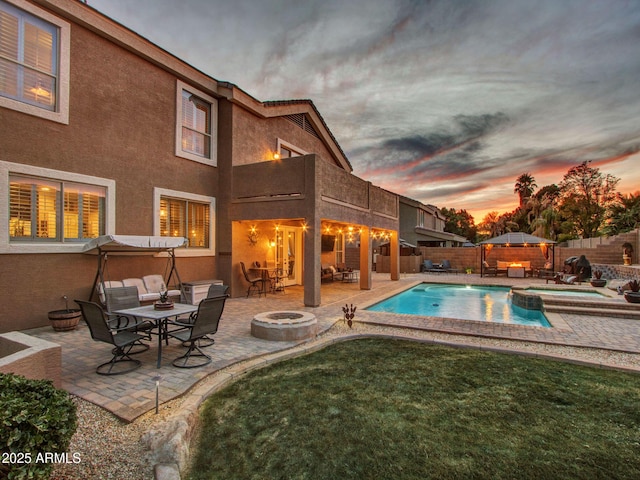 pool at dusk featuring an in ground hot tub, an outdoor fire pit, and a patio