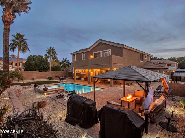 pool at dusk with a gazebo, grilling area, a patio, and an outdoor fire pit