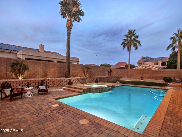 pool at dusk featuring an in ground hot tub and a patio area