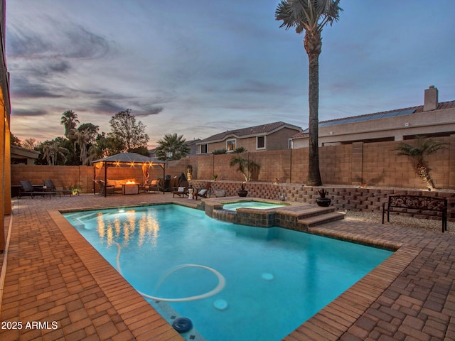 pool at dusk featuring a gazebo, an in ground hot tub, and a patio area