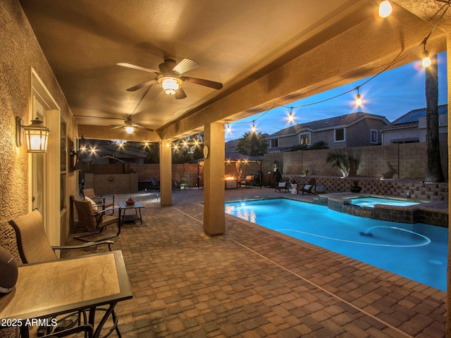 pool at dusk featuring an in ground hot tub, ceiling fan, and a patio