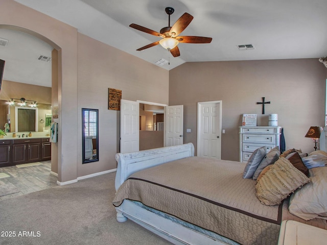 bedroom featuring ceiling fan, light colored carpet, high vaulted ceiling, and ensuite bath