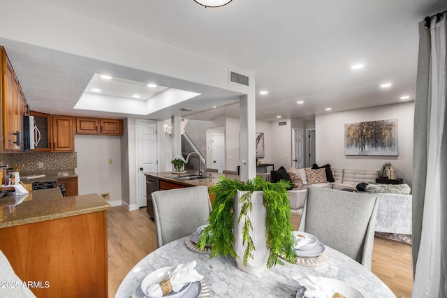 dining room featuring a tray ceiling, sink, and light hardwood / wood-style flooring